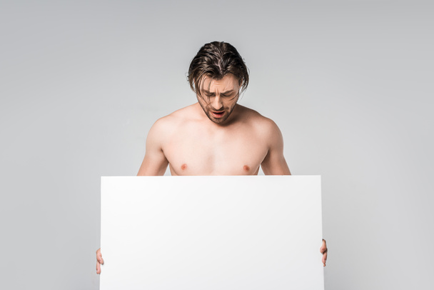 портрет красивого без сорочки чоловіка, який дивиться на порожній банер в руках ізольований на сірому
 - Фото, зображення