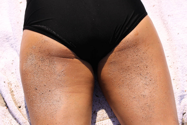 Vista trasera de la chica acostada en la playa de arena con arena en los muslos
  - Foto, imagen