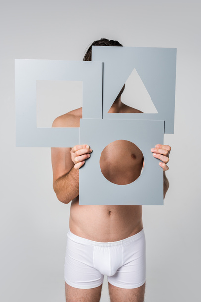 obscured view of man in underwear holding grey paper figures in hands isolated on grey - Photo, Image