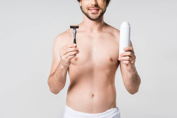 partial view of smiling man in white towel with razor and shaving foam in hands isolated on grey - Fotografie, Obrázek