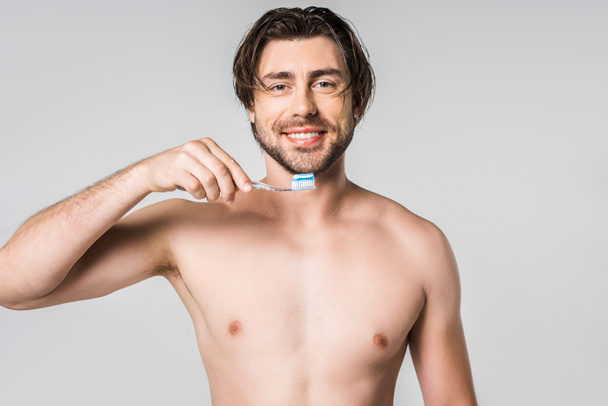 retrato de homem sem camisa sorridente com escova de dentes isolada em cinza
 - Foto, Imagem