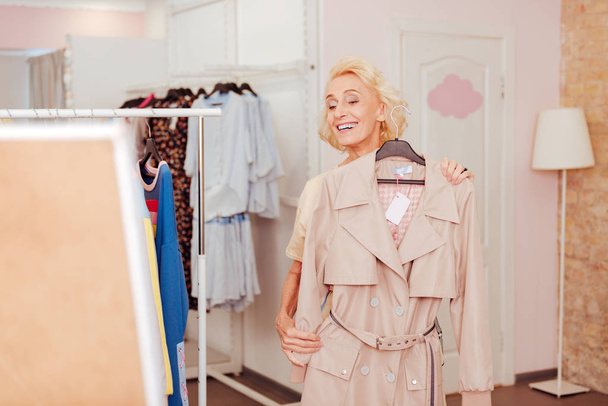 Blonde-haired retired woman smiling while buying new clothes - Foto, afbeelding