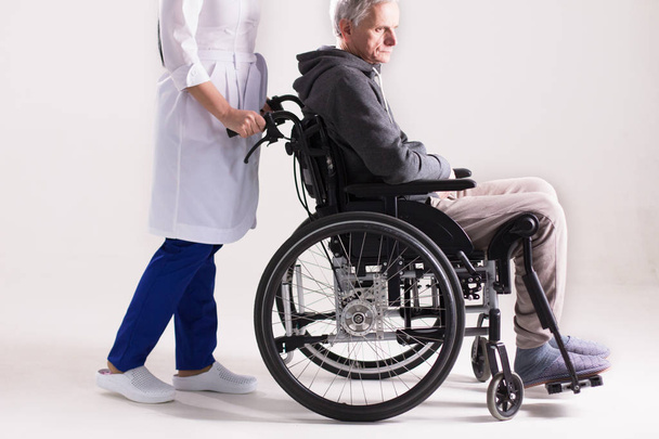 Nurse pushing wheelchair with man in it. - Zdjęcie, obraz