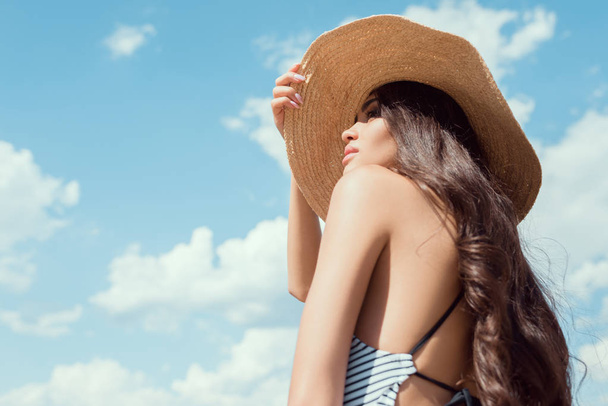 attractive brunette girl posing in straw hat with blue sky on background - Foto, afbeelding