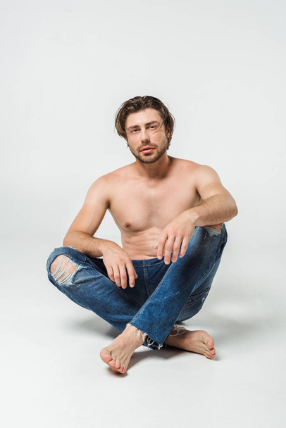 pensive shirtless man in jeans looking at camera on grey backdrop - Foto, afbeelding