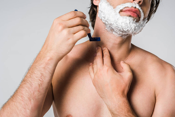 cropped shot of shirtless man with foam on face shaving beard isolated on grey - Фото, зображення