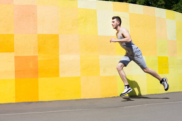 Young man running against bright wall - Φωτογραφία, εικόνα
