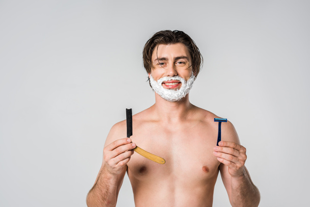 retrato del hombre sonriente con espuma de afeitar en la cara que sostiene las cuchillas aisladas en gris
 - Foto, imagen