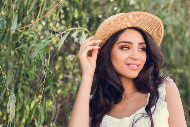 柳の木に近いポーズ麦わら帽子の美しい若い女性 - 写真・画像
