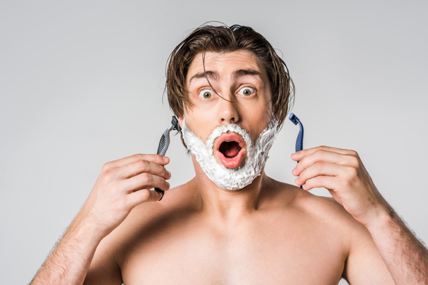 portrait of shocked man with shaving foam on face holding razors isolated on grey - Foto, Imagen