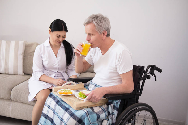 Pielęgniarka, przynosząc żywność do pacjenta na wózku inwalidzkim. - Zdjęcie, obraz