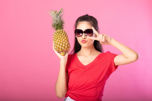 Attractive happy young woman holding fresh pineapple with cute kiss. Isolated over pink background. Summer lifestyle concept. - Fotoğraf, Görsel