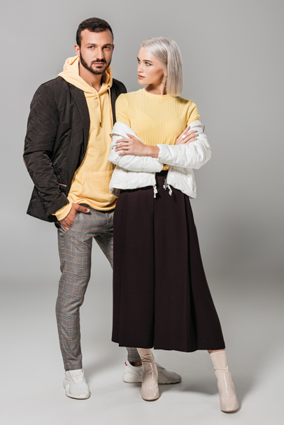 young stylish female model with crossed arms standing with boyfriend on grey background  - Φωτογραφία, εικόνα