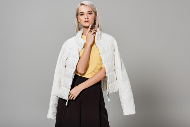 zeker jonge vrouwelijke model in witte jas over schouders poseren geïsoleerd op een grijze achtergrond - Foto, afbeelding