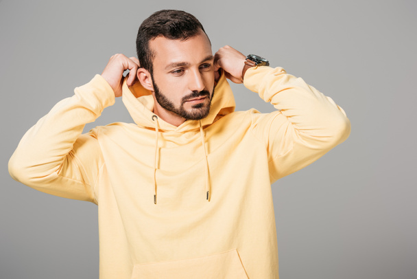 handsome bearded male model putting on yellow hoodie isolated on grey background  - Photo, Image