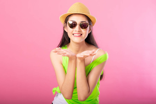 Portrait of a smiling attractive woman in green summer outfit and hat posing while standing and looking at camera isolated over pink background. - Foto, imagen