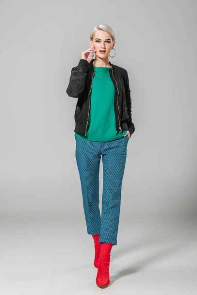 fashionable woman in black jacket and red boots posing on grey background  - Photo, image
