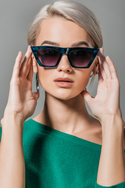 молода стильна дівчина в сонцезахисних окулярах і зелений светр дивиться на камеру ізольовано на сірому фоні
  - Фото, зображення