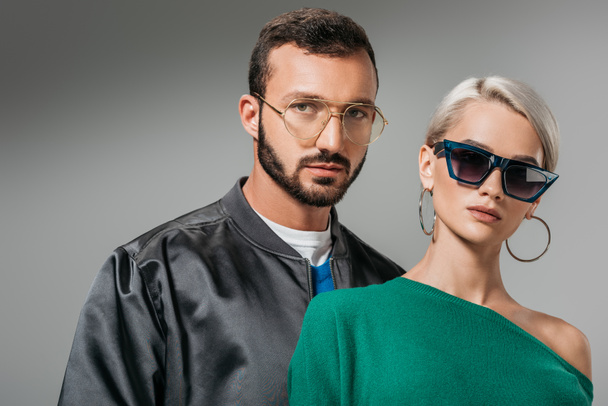 fashionable couple posing in eyeglasses and sunglasses, isolated on grey - Foto, afbeelding