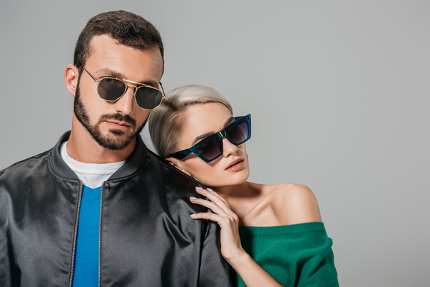 stylish couple posing in sunglasses for fashion shoot, isolated on grey - Fotó, kép