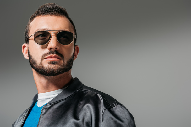 bearded man posing in black bomber and sunglasses,  isolated on grey - 写真・画像