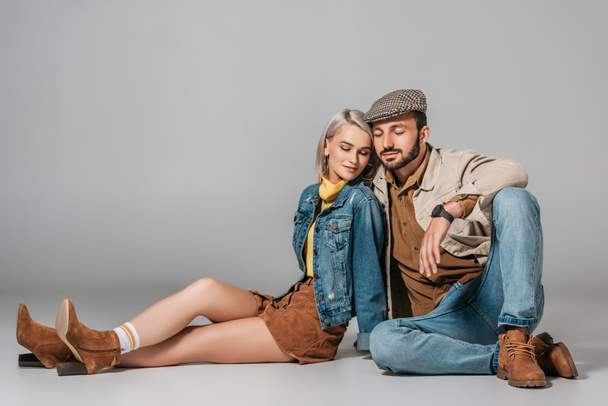 happy couple in autumn outfit sitting on floor, on grey - Foto, imagen