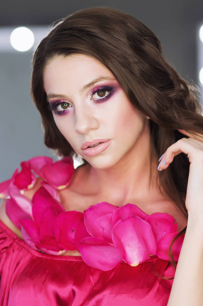 Vista de la cosecha de atractiva hembra con el pelo ondulado lápiz labial rosa y sombras de ojos posando en la cámara sobre fondo borroso
 - Foto, Imagen