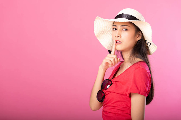Portrait of attractive woman in summer outfit and hat posing secret hush while standing and looking at camera isolated over pink background. - Valokuva, kuva