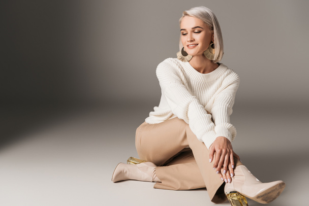 Lächelndes elegantes Model posiert in weißem Pullover, beiger Hose und Herbst-Heels, auf grau  - Foto, Bild