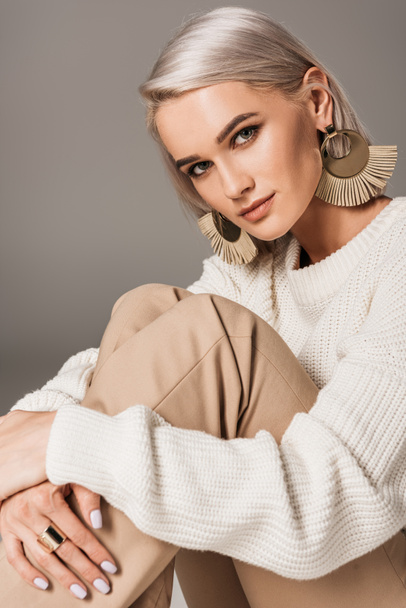 elegant stylish woman in white sweater and big earrings looking at camera, isolated on grey - Photo, Image