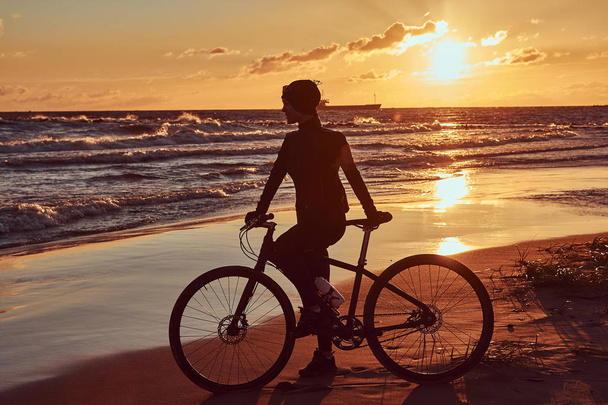 Femme cycliste debout avec son vélo et profiter du coucher de soleil sur la côte de la mer
. - Photo, image