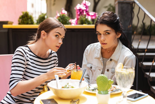 Geheime alcohol. Twee jonge vrouwen in het geheim toe te voegen alcohol uit kleine fles aan hun cocktail van restaurant - Foto, afbeelding