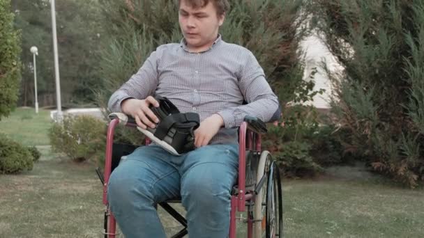 Niepełnosprawny mężczyzna w fotelu inwalidzkim usuwa kask wirtualnej rzeczywistości - Materiał filmowy, wideo