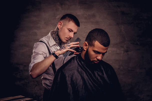 Bearded African American hipster guy getting a haircut by an old-fashioned tattoed professional hairdresser does the haircut. - Photo, Image