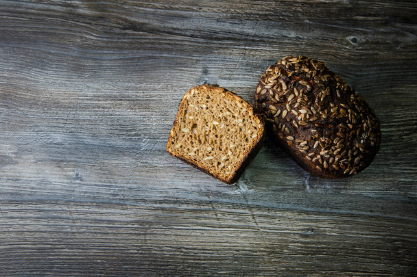 whole and half of delicious homemade rectangular rye bread with sunflower seeds on dark table background - Photo, Image