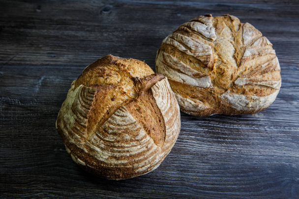 two whole tasty handmade round white wheat bread lie on dark wooden table - Фото, зображення
