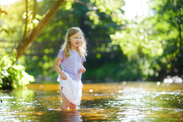 Cute little girl playing by a river on hot summer day. Adorable child having fun outdoors during summer vacations. Water activities for kids. - Foto, imagen