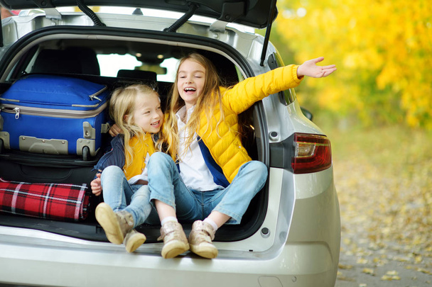 Two adorable girls with a suitcase going on vacations with their parents. Two kids looking forward for a road trip or travel. Autumn break at school. Family travel by car. - Foto, Bild