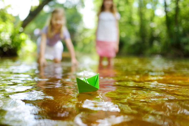 Two little sisters playing with paper boats by a river on warm and sunny summer day. Children having fun by the water. Summer activities for small kids. - Foto, imagen
