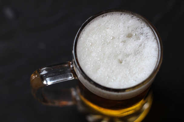 Light bier met een witte pluizige schuim op een donkere achtergrond - Foto, afbeelding