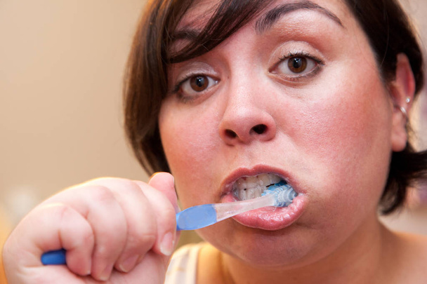 A very close to the face portrait of a woman brushing her teeth looking surprised  - Foto, immagini