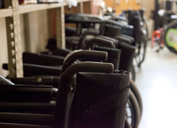 Zwarte rolstoelen met handvatten opgesteld in een onderwijs-kliniek of klaar voor gebruik in een ziekenhuis  - Foto, afbeelding