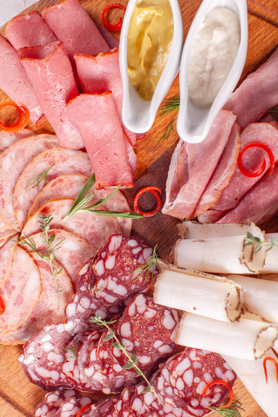 Plato de carne ahumada fría con cerdo, jamón, salami sobre fondo de madera. Salsa de mostaza y crema de ajo
 - Foto, Imagen