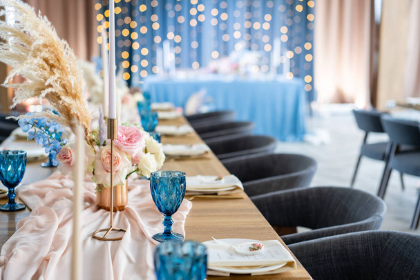 Весільний бенкет або гала-вечеря. Стільці та стіл для гостей, подаються з столовими приборами та посудом. Покритий пастельно-рожевою скатертиною бігун. вечірка освітлена гірляндами
 - Фото, зображення