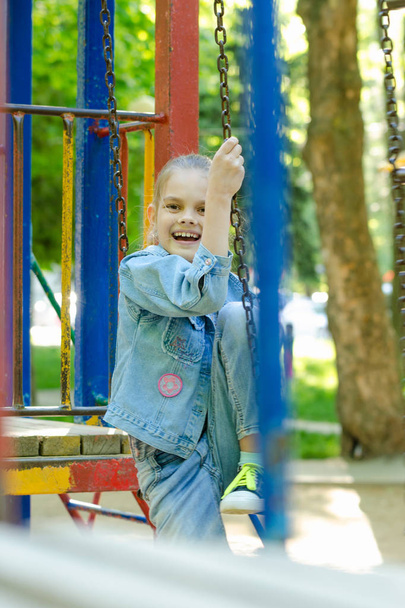 A menina alegre e fervorosamente ri sentado em uma escada pendurada no playground
 - Foto, Imagem