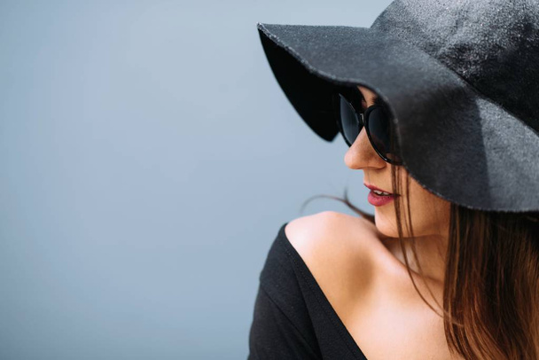 Όμορφη κοπέλα σε ένα μαύρο καπέλο θέτει το υπόβαθρο του τοίχου. - Φωτογραφία, εικόνα