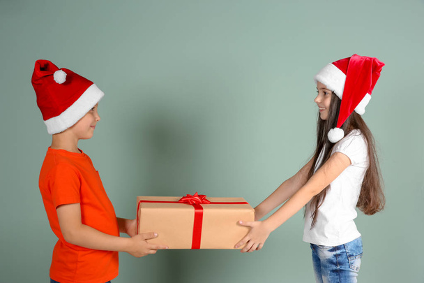 Cute little children in Santa hats with Christmas gift box on color background - Foto, imagen