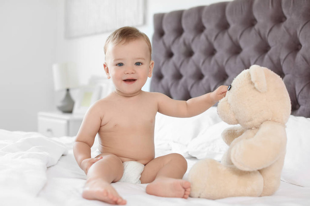 Adorable little baby with teddy bear on bed at home - Fotó, kép