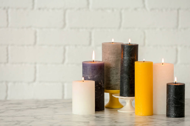 Different decorative wax candles on table against brick wall - Foto, Imagem