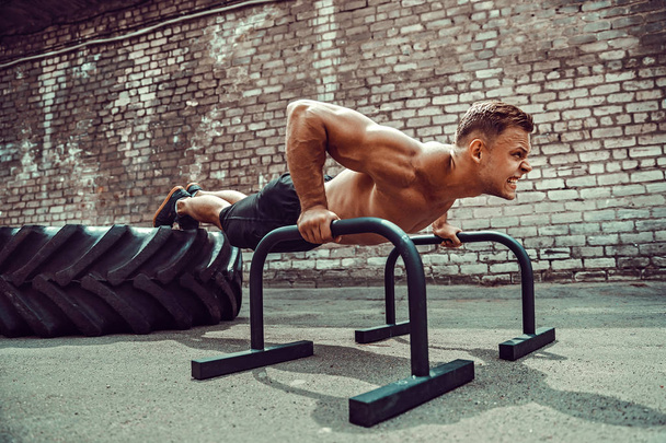 Strong sporty happy cheerful positive man doing press exercises holding plank outdoors - Zdjęcie, obraz